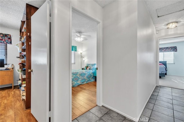 corridor with baseboards, light tile patterned flooring, and a textured ceiling