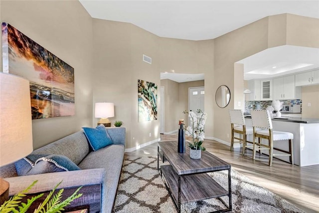 living area featuring baseboards, light wood-style flooring, visible vents, and a high ceiling