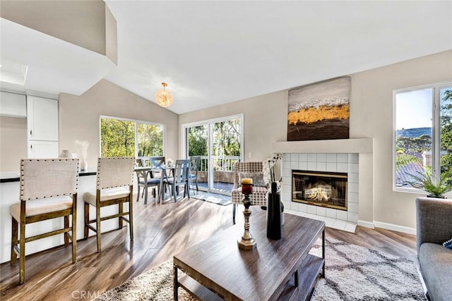 living area with baseboards, lofted ceiling, light wood finished floors, and a tiled fireplace