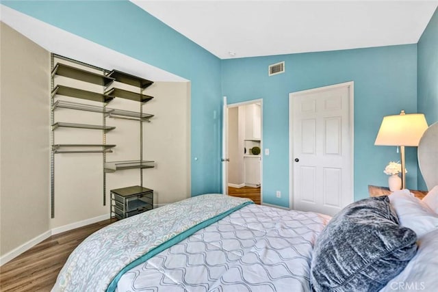 bedroom featuring baseboards, wood finished floors, visible vents, and a closet