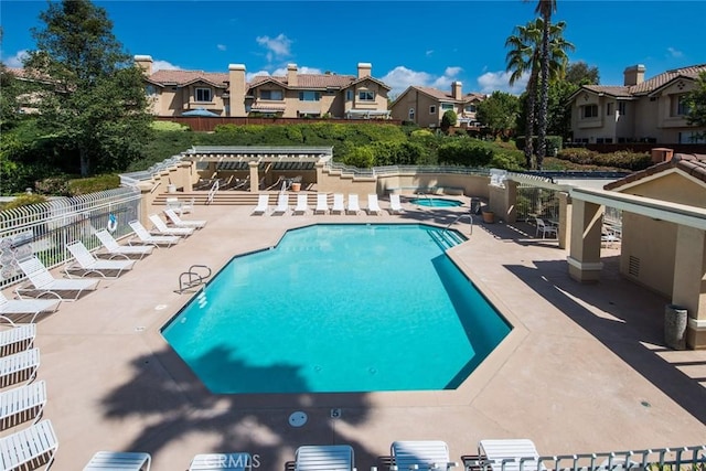 pool featuring a community hot tub, a residential view, a patio area, and fence