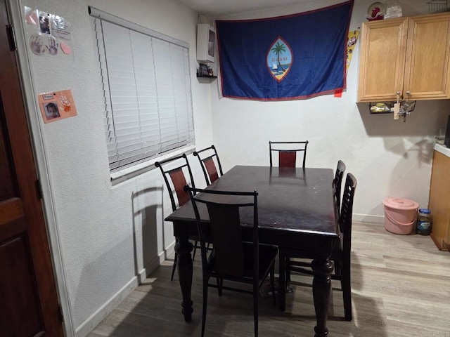 dining space featuring a textured wall, baseboards, and wood finished floors