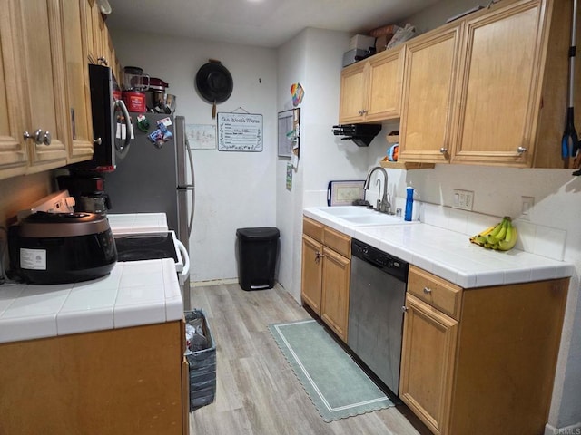 kitchen with stainless steel dishwasher, light wood finished floors, tile countertops, and a sink