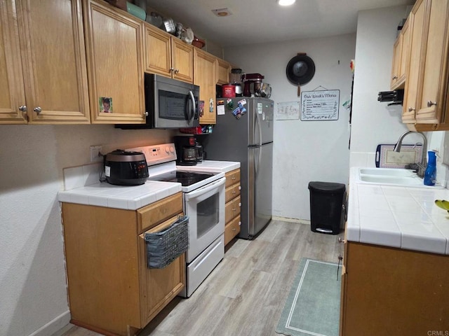 kitchen featuring tile counters, light wood-style flooring, appliances with stainless steel finishes, a sink, and baseboards