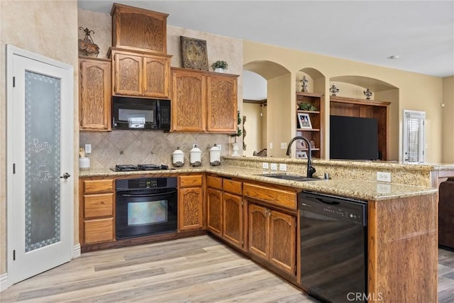 kitchen featuring tasteful backsplash, a peninsula, black appliances, light wood finished floors, and a sink