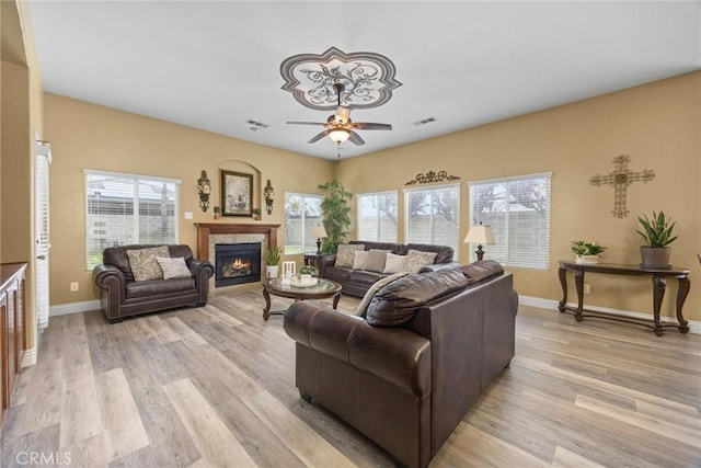 living room with a lit fireplace, light wood-type flooring, baseboards, and a ceiling fan