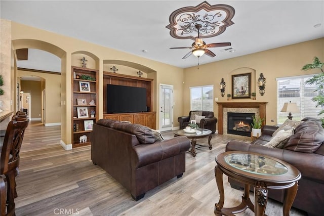 living room featuring a glass covered fireplace, light wood-style flooring, visible vents, ceiling fan, and arched walkways