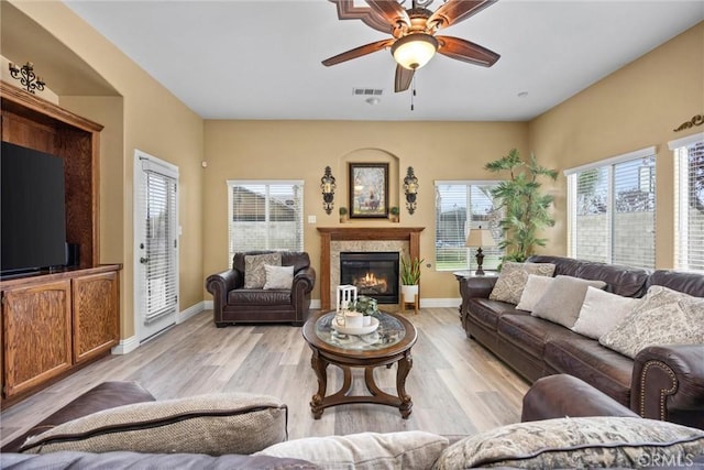 living room featuring visible vents, baseboards, a ceiling fan, light wood-style floors, and a glass covered fireplace