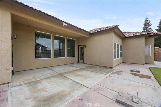 rear view of property featuring a tile roof, a patio, and stucco siding