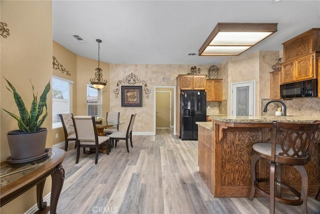 kitchen with light wood-style floors, visible vents, black appliances, baseboards, and backsplash