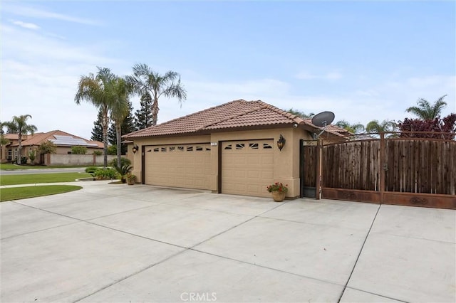 view of side of property with stucco siding, driveway, an attached garage, a tile roof, and fence