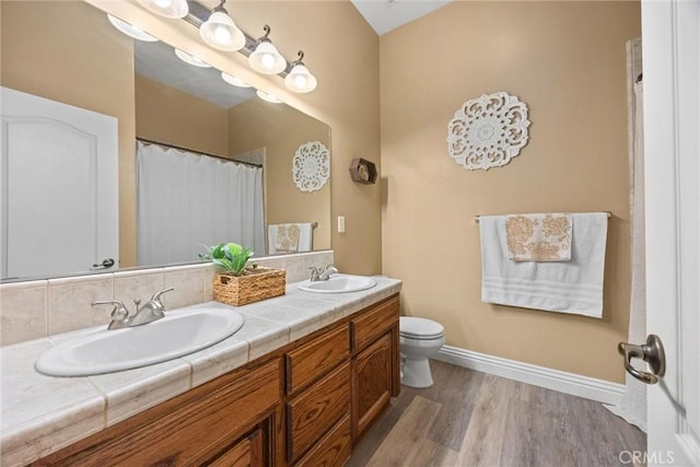 full bathroom with double vanity, baseboards, a sink, and wood finished floors