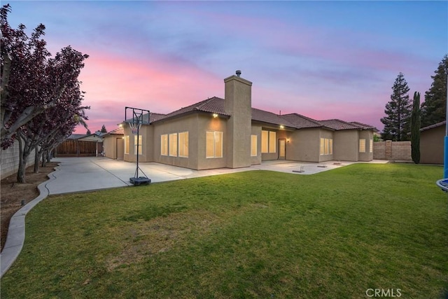 back of property at dusk with a patio, a fenced backyard, a chimney, and a lawn