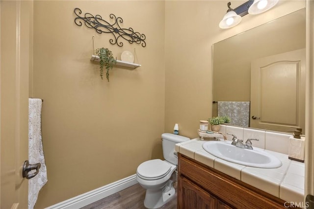 bathroom with toilet, wood finished floors, vanity, and baseboards