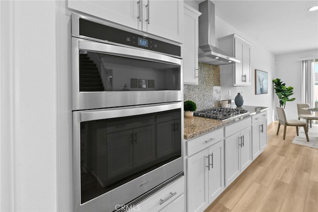 29553 Tulipwood St, Menifee, CA 92584 - kitchen with wall chimney range hood, light wood-style flooring, backsplash, white cabinets, and stainless steel appliances
