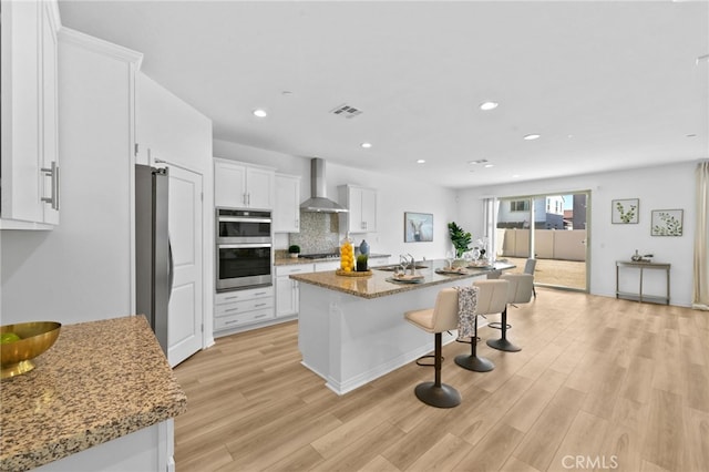 29553 Tulipwood St, Menifee, CA 92584 - kitchen featuring white cabinets, wall chimney exhaust hood, light wood-type flooring, a kitchen breakfast bar, and stainless steel appliances