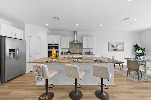 29553 Tulipwood St, Menifee, CA 92584 - kitchen with visible vents, wall chimney range hood, a kitchen bar, light wood finished floors, and stainless steel appliances