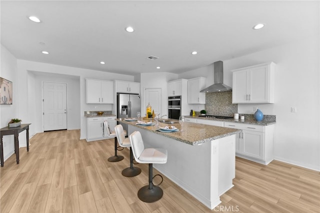 29553 Tulipwood St, Menifee, CA 92584 - kitchen with light wood finished floors, wall chimney range hood, white cabinets, and stainless steel appliances