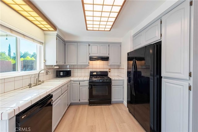 kitchen featuring under cabinet range hood, tile countertops, a sink, and black appliances