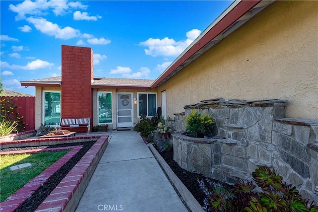 property entrance with a chimney, stucco siding, and fence