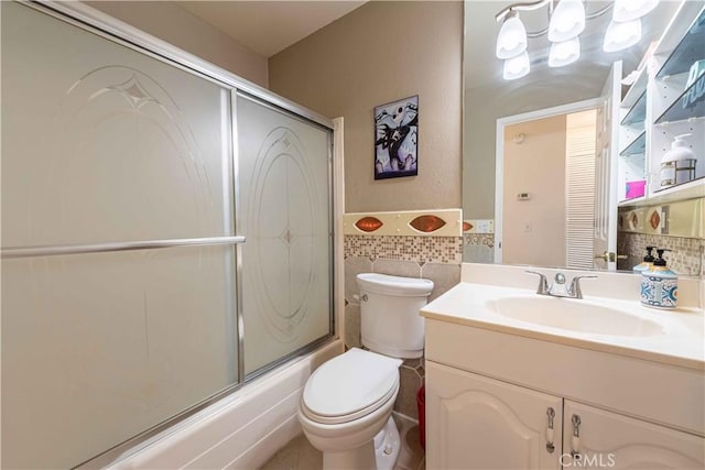 full bathroom featuring bath / shower combo with glass door, toilet, tile walls, vanity, and wainscoting
