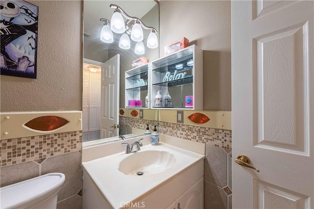 bathroom featuring toilet, vanity, a wainscoted wall, and tile walls