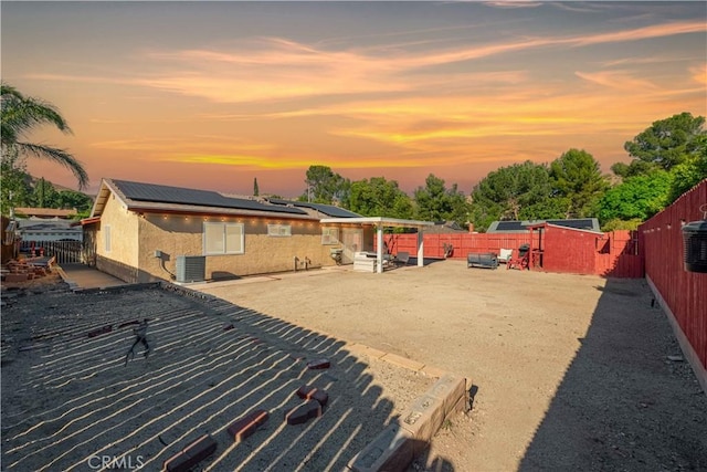 back of property with stucco siding, a patio area, a fenced backyard, central AC, and roof mounted solar panels