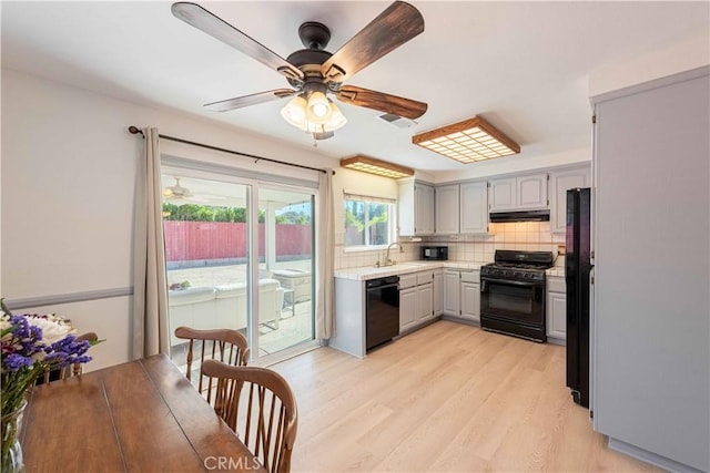 kitchen with tasteful backsplash, a sink, under cabinet range hood, black appliances, and gray cabinetry