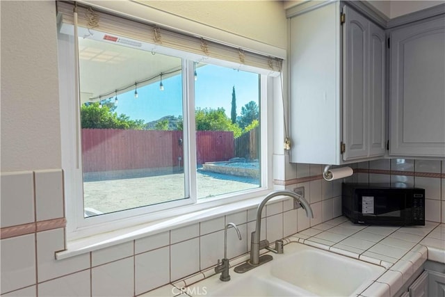 kitchen with black microwave, gray cabinets, a sink, and decorative backsplash