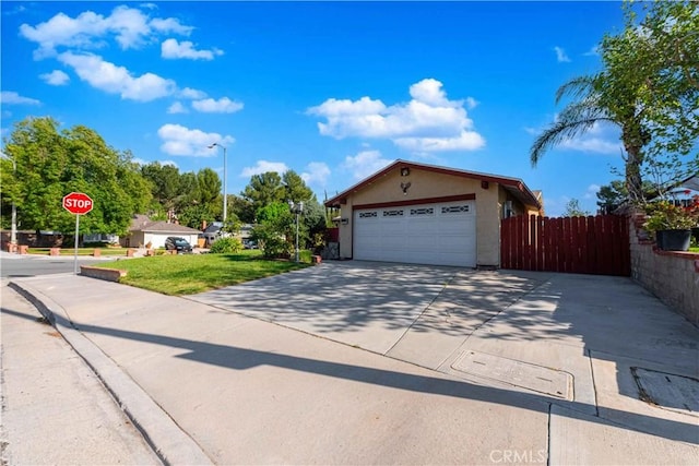 view of front of home featuring concrete driveway, stucco siding, a front lawn, a garage, and fence