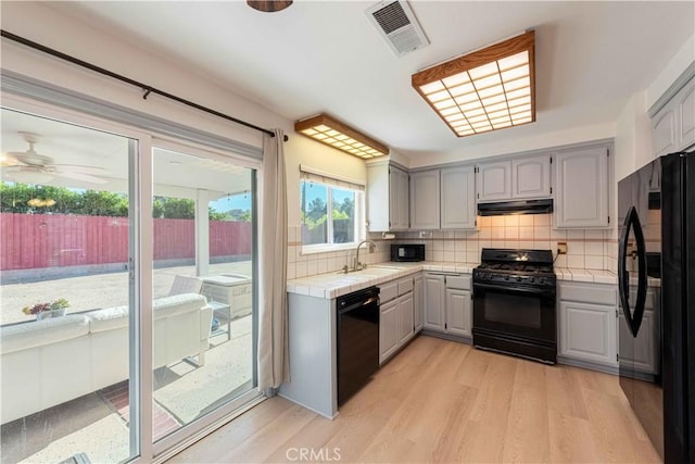 kitchen with under cabinet range hood, visible vents, tile counters, and black appliances