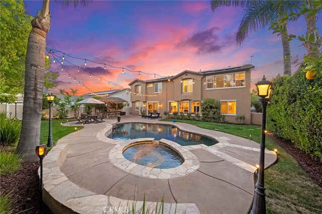 back of house at dusk with a patio, stucco siding, a yard, and fence