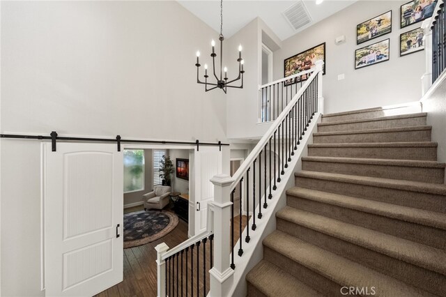 staircase with visible vents, hardwood / wood-style floors, a high ceiling, a barn door, and a chandelier