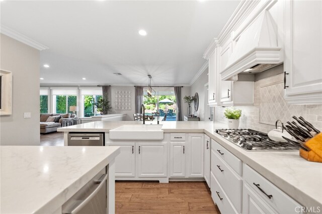 kitchen featuring a peninsula, custom exhaust hood, recessed lighting, a sink, and appliances with stainless steel finishes