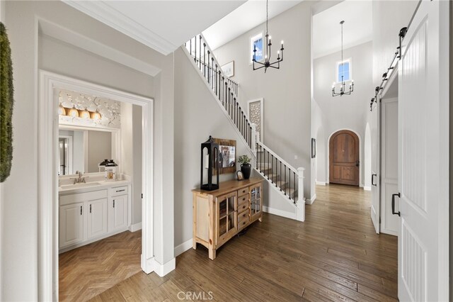 foyer with an inviting chandelier, arched walkways, baseboards, a towering ceiling, and stairway