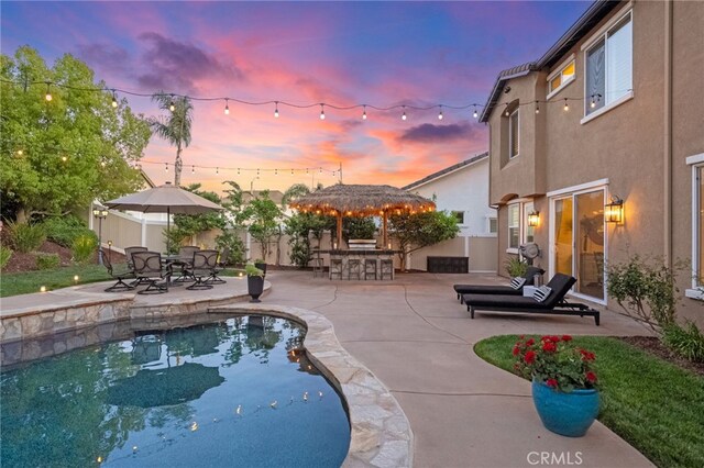 pool at dusk with a fenced backyard, outdoor dry bar, a patio, and a fenced in pool