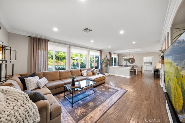 living room with a wealth of natural light, ornamental molding, a chandelier, and visible vents