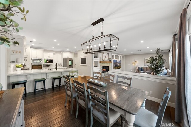 dining room with a lit fireplace, recessed lighting, a chandelier, and dark wood-type flooring