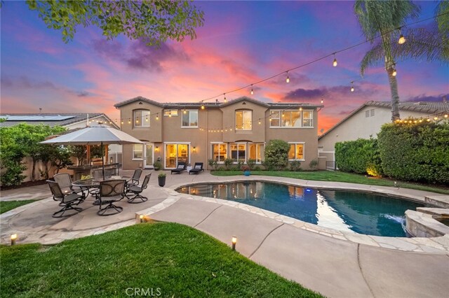 back of house at dusk featuring a patio, a fenced in pool, fence, and stucco siding