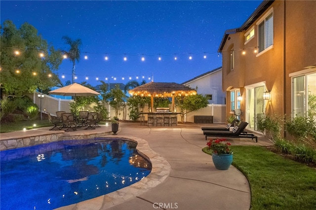 pool at night with a fenced backyard, a patio area, and outdoor dry bar