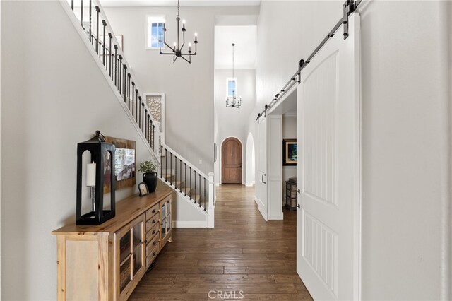foyer with a towering ceiling, arched walkways, a barn door, an inviting chandelier, and dark wood-type flooring