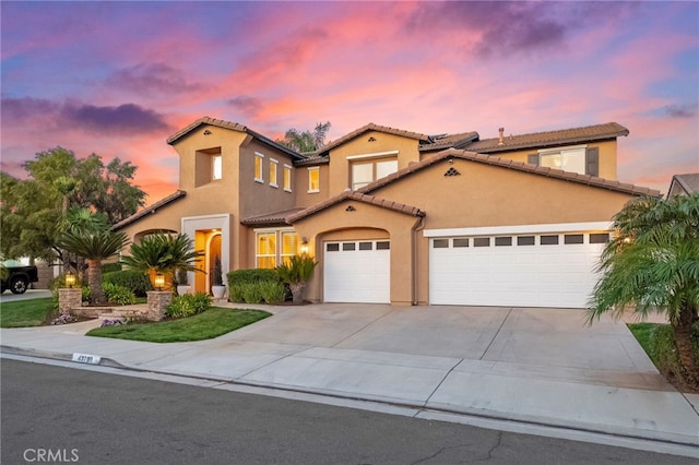 mediterranean / spanish home with an attached garage, concrete driveway, stucco siding, and a tiled roof