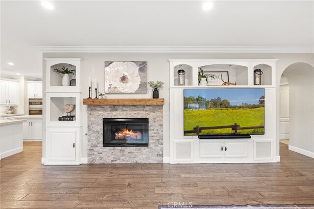 living room with arched walkways, wood finished floors, a glass covered fireplace, ornamental molding, and recessed lighting