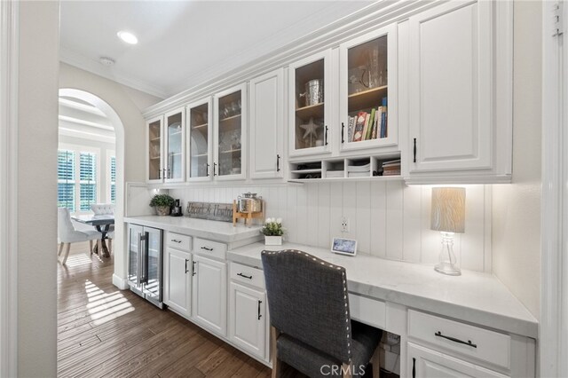 bar with crown molding, built in desk, beverage cooler, arched walkways, and dark wood-type flooring