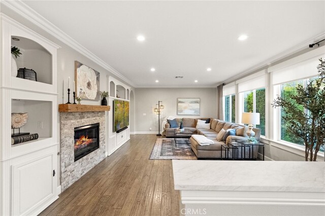 living room with crown molding, wood finished floors, baseboards, a glass covered fireplace, and recessed lighting
