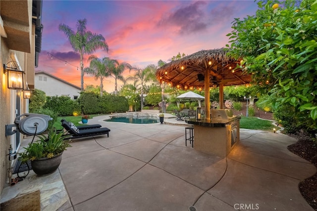 patio terrace at dusk featuring a fenced in pool, outdoor dry bar, and a gazebo