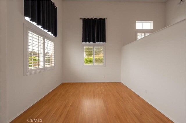 spare room with baseboards, a high ceiling, light wood-style floors, and a healthy amount of sunlight