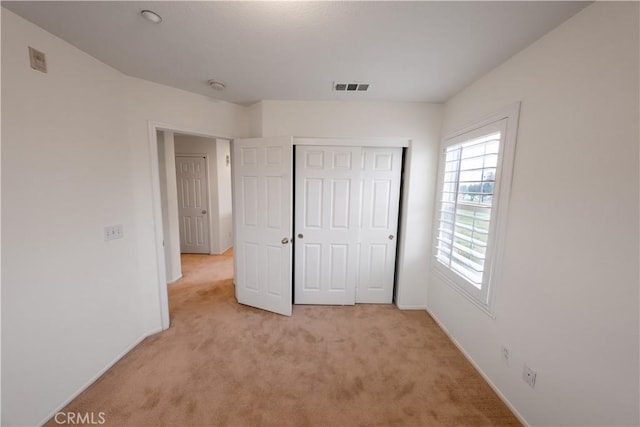 unfurnished bedroom with baseboards, light carpet, visible vents, and a closet