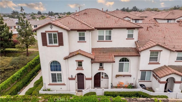 mediterranean / spanish-style house with stucco siding, a tiled roof, and a fenced front yard
