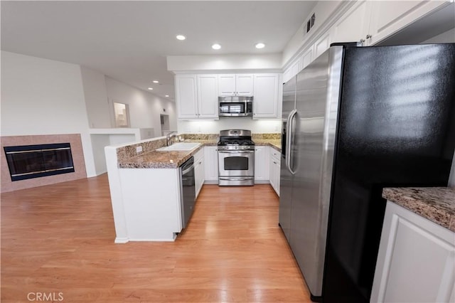 kitchen with a peninsula, stainless steel appliances, light wood finished floors, and a sink